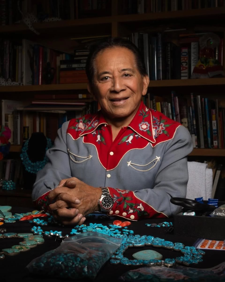 Federico Jimenez seated at his worktable surrounded by turquoise and silver, with a wall of books behind him.